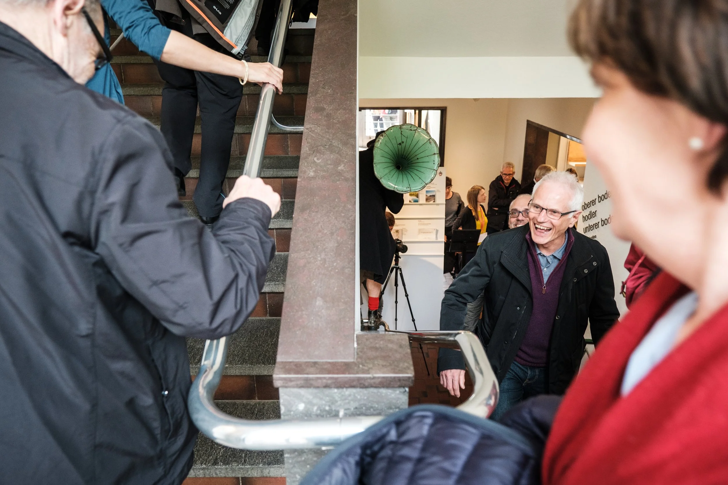 Lachen und freundliche Interaktion zwischen Menschen auf einer Treppe in einem Wartebereich.