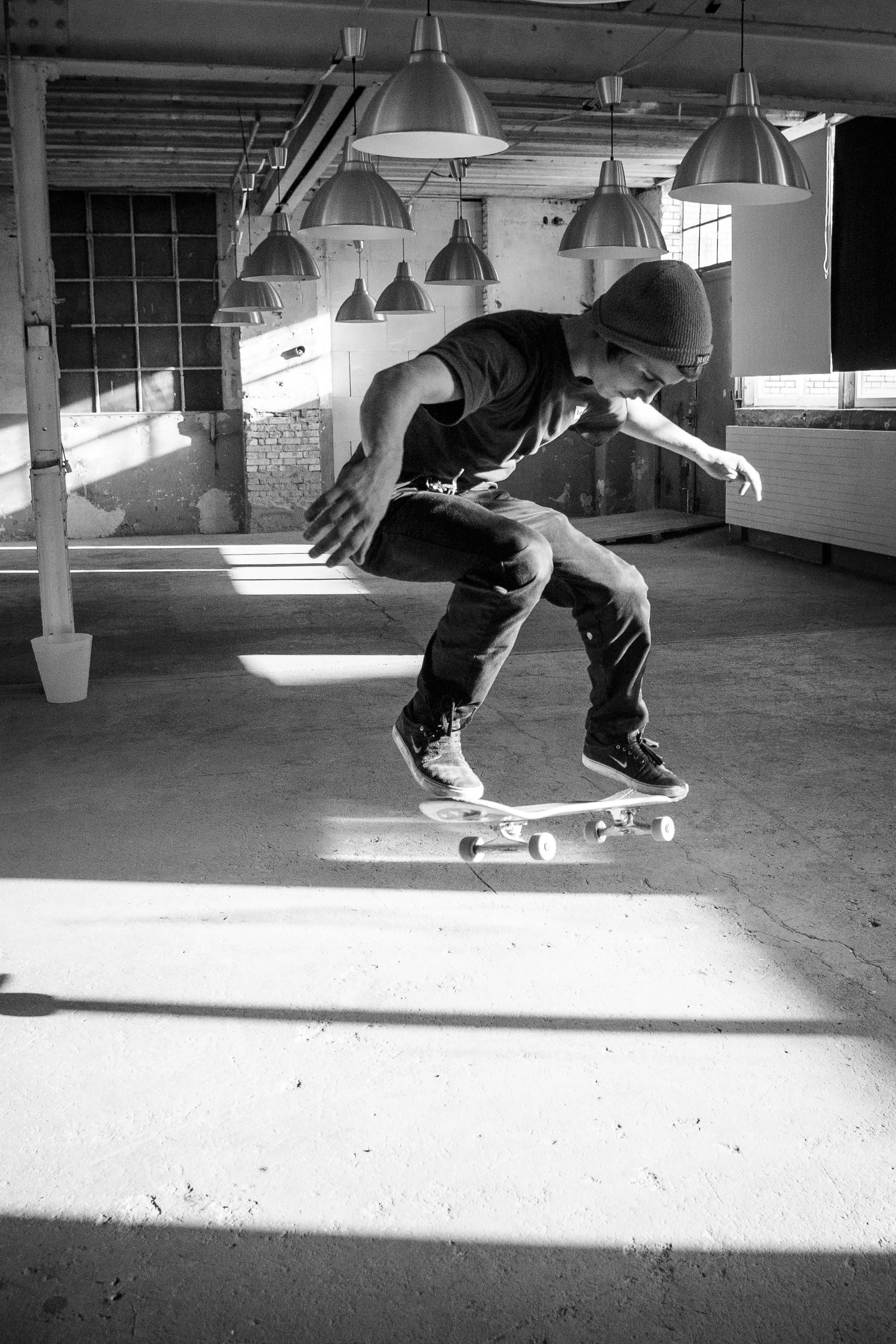 Ein junger Mann, der auf einem Skateboard in einem industrialen Raum im Schwarz-Weiß-Bild tricks macht.