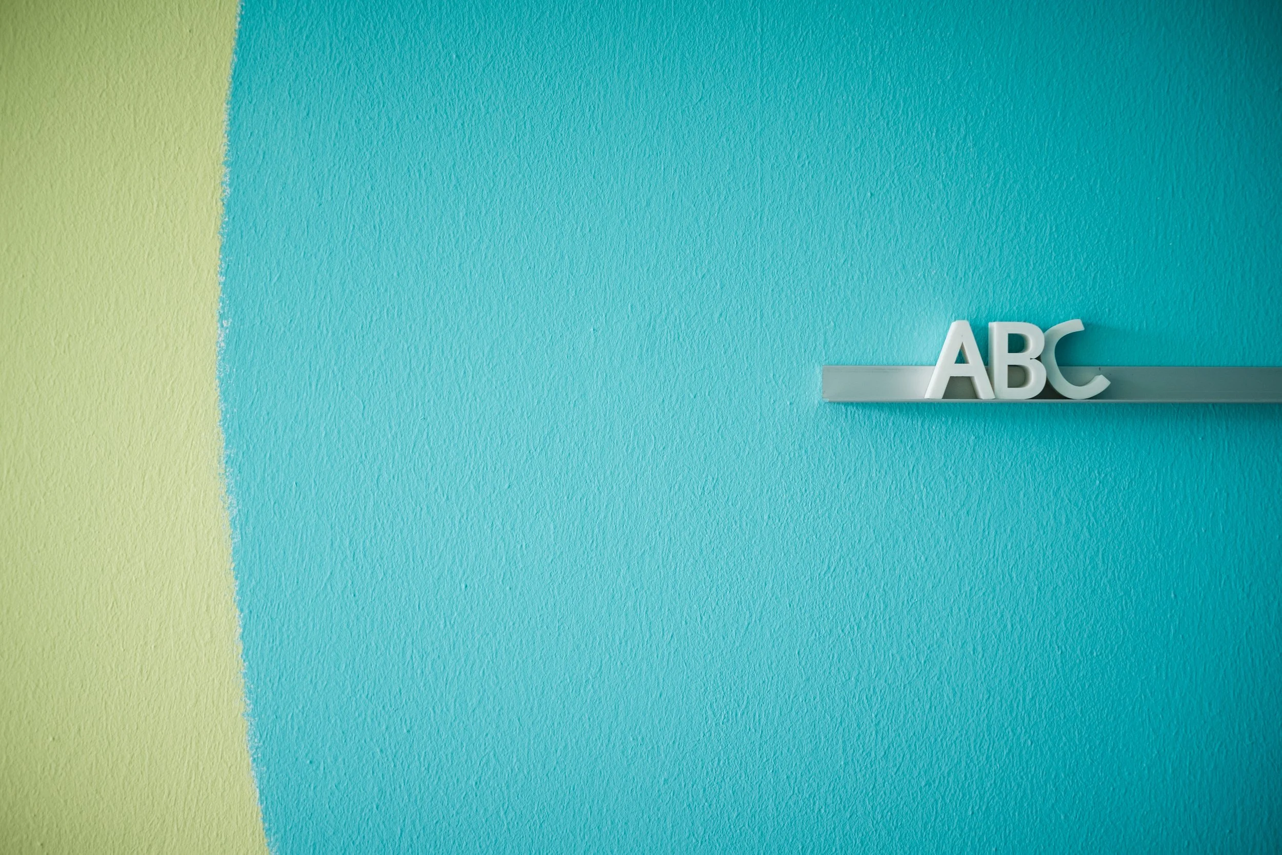 Bunte Wand mit blauem, grünem und gelbem Farbabschnitt und weiße Dekoration mit den Buchstaben ABC.