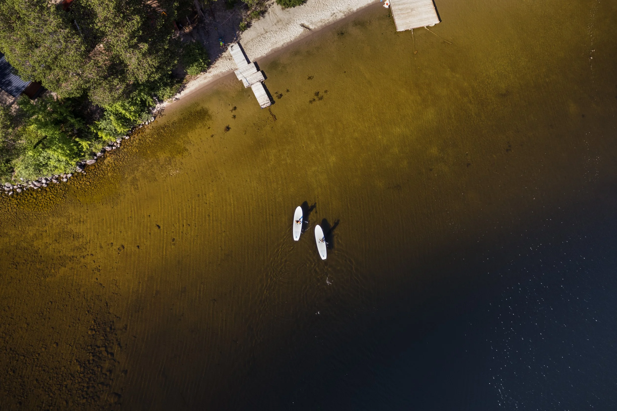 Vogelperspektive auf einen Strand mit Booten im Wasser und Bäumen am Ufer.